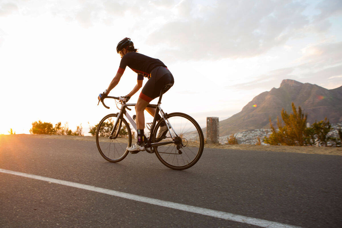 Female cyclist riding a road bike during sunset on a scenic mountain road.