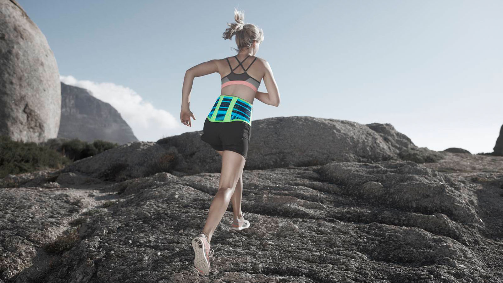 Woman trail running on rocky terrain wearing fitness attire with back support belt