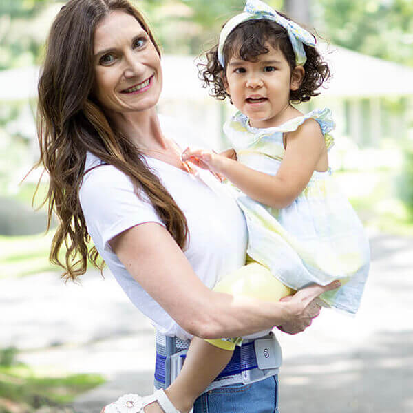 Smiling mother holding her child while wearing Bauerfeind's SacroLoc SI joint belt.