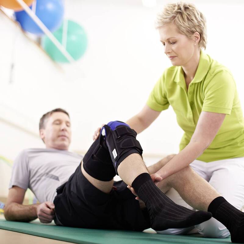 Physical therapist assisting a male patient with knee brace adjustment in clinic