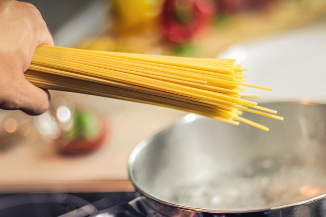 Uncooked spaghetti noodles being held over a boiling pot of water.