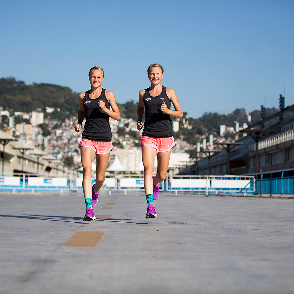 Two women jogging outdoors in brightly colored athletic wear.