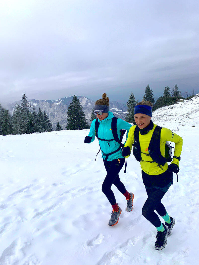 Two women running through snowy weather while wearing cold weather gear.