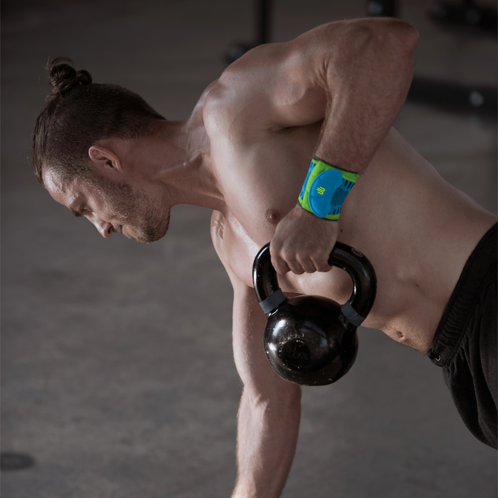 Man performing kettlebell row exercise while wearing Bauerfeind's Sports Wrist Strap in a fitness center.