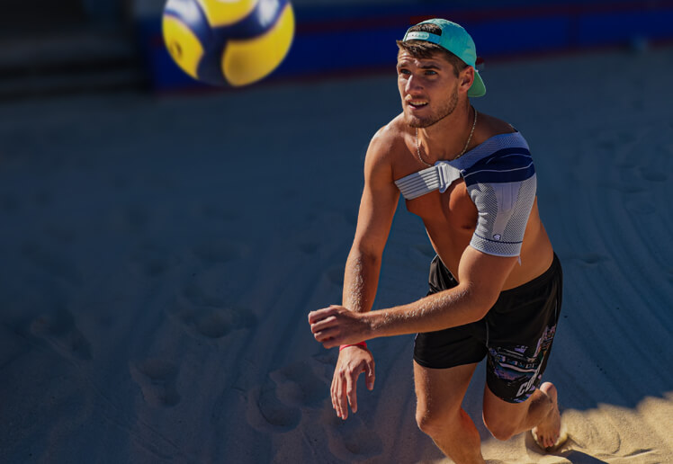 Male athlete competing in beach volleyball while wearing Bauerfeind's OmoTrain S shoulder brace.