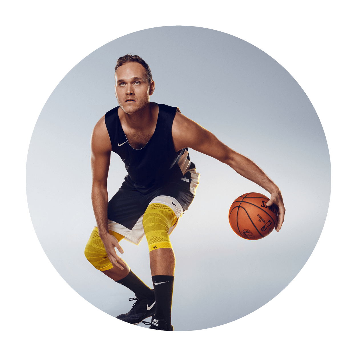 Athlete dribbling a basketball while wearing Bauerfeind's Sports Compression Knee Support NBA Lakers Edition.