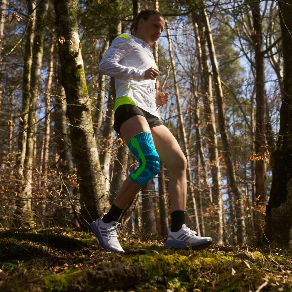 Woman jogging in the forest with a knee brace, wearing athletic gear.