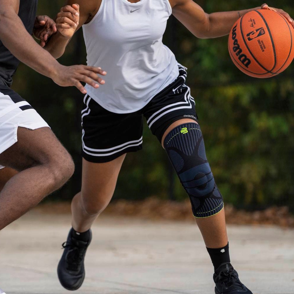 Close-up of two basketball players during a game, one wearing a knee brace and holding a basketball.