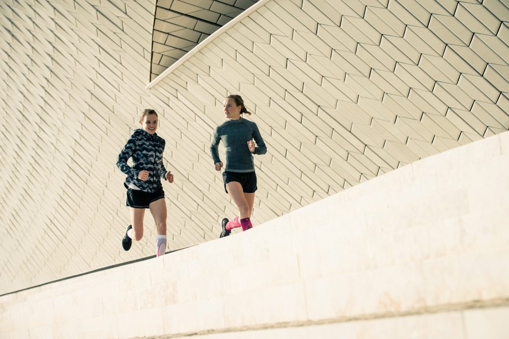 Woman wearing Bauerfeind's Run Performance Compression Socks while running through a city street.