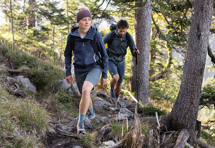 Two hikers wearing a pair of Bauerfeind's Outdoor Merino Mid Cut Socks while trekking through a narrow rocky trail.