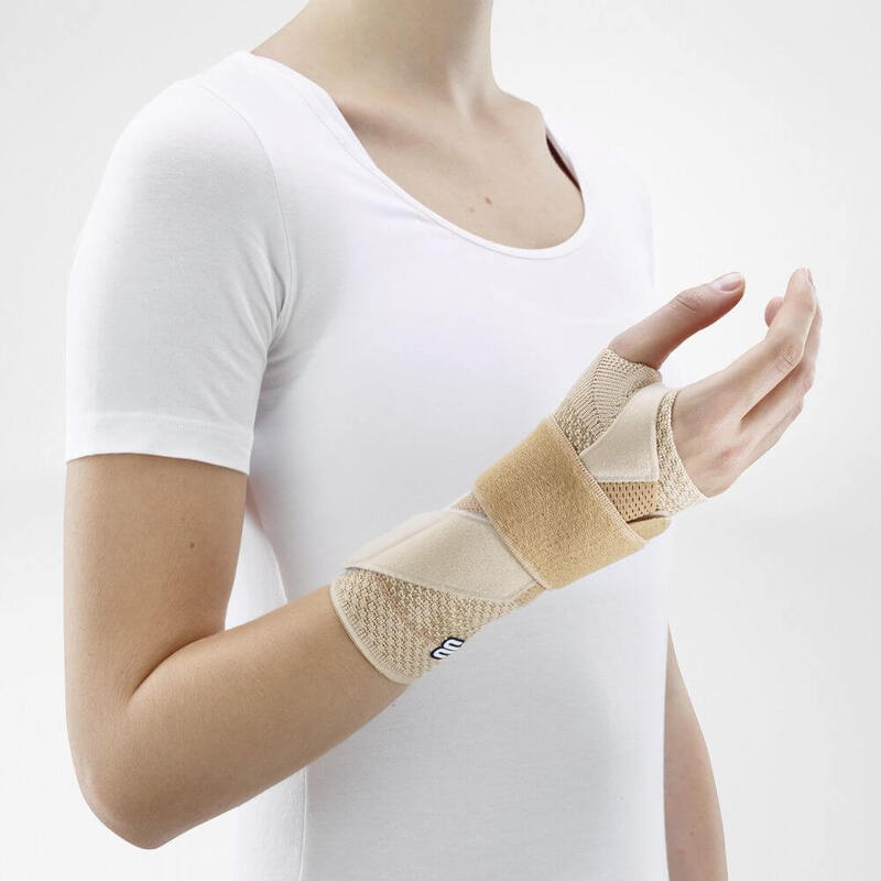 Woman wearing Bauerfeind's ManuTrain wrist brace (beige) while standing in front of a gray background.