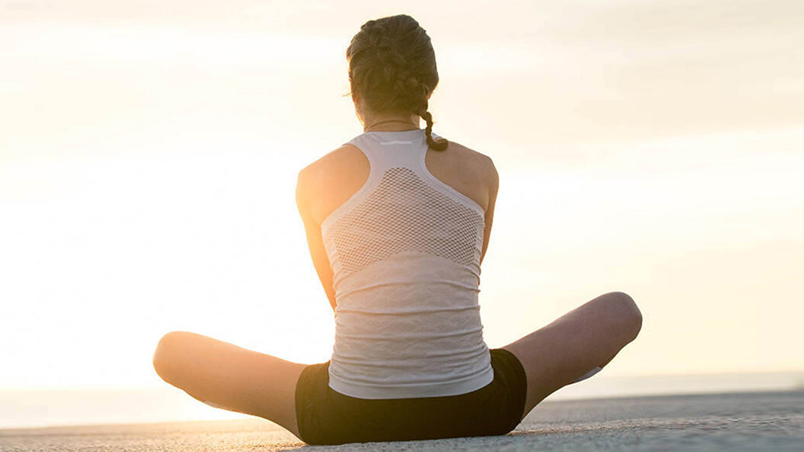 Woman performing a seated leg and hip stretch before her morning run by the ocean.