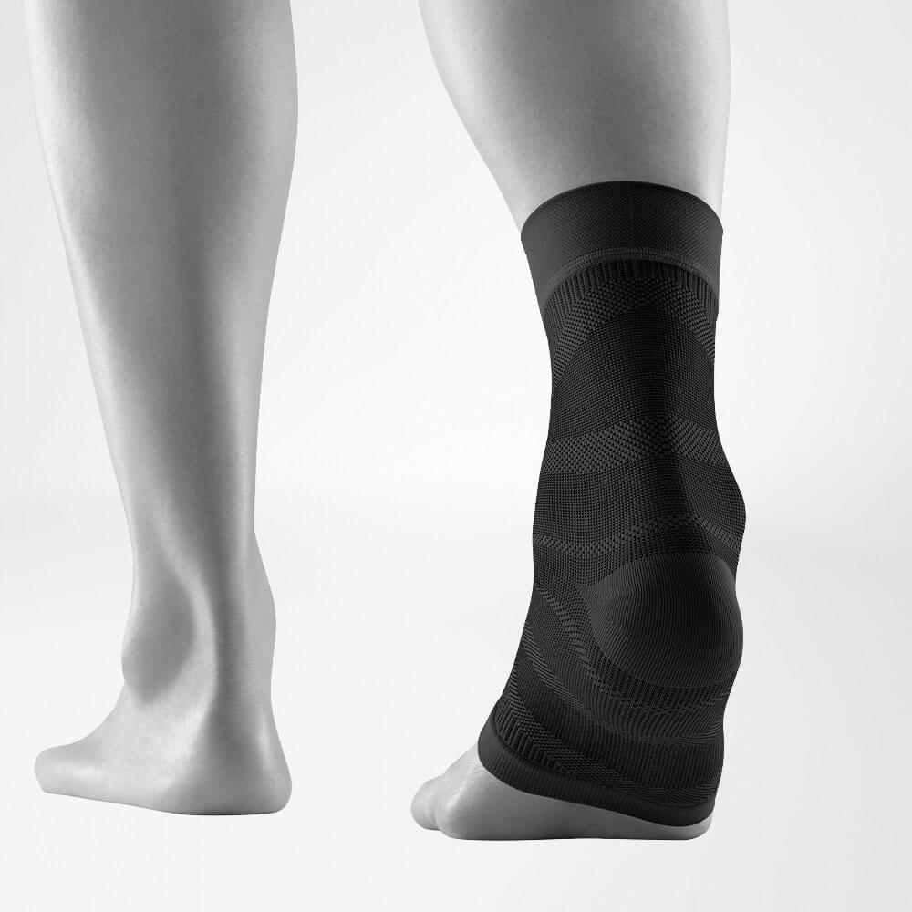 Close-up of a black ankle compression sleeve worn on a person's left foot and ankle, providing support and stability.