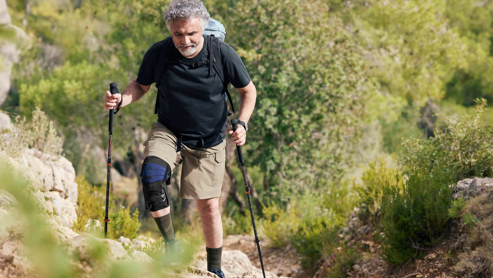 Senior man stretching on the beach while wearing Bauerfeind's GenuTrain OA knee brace.