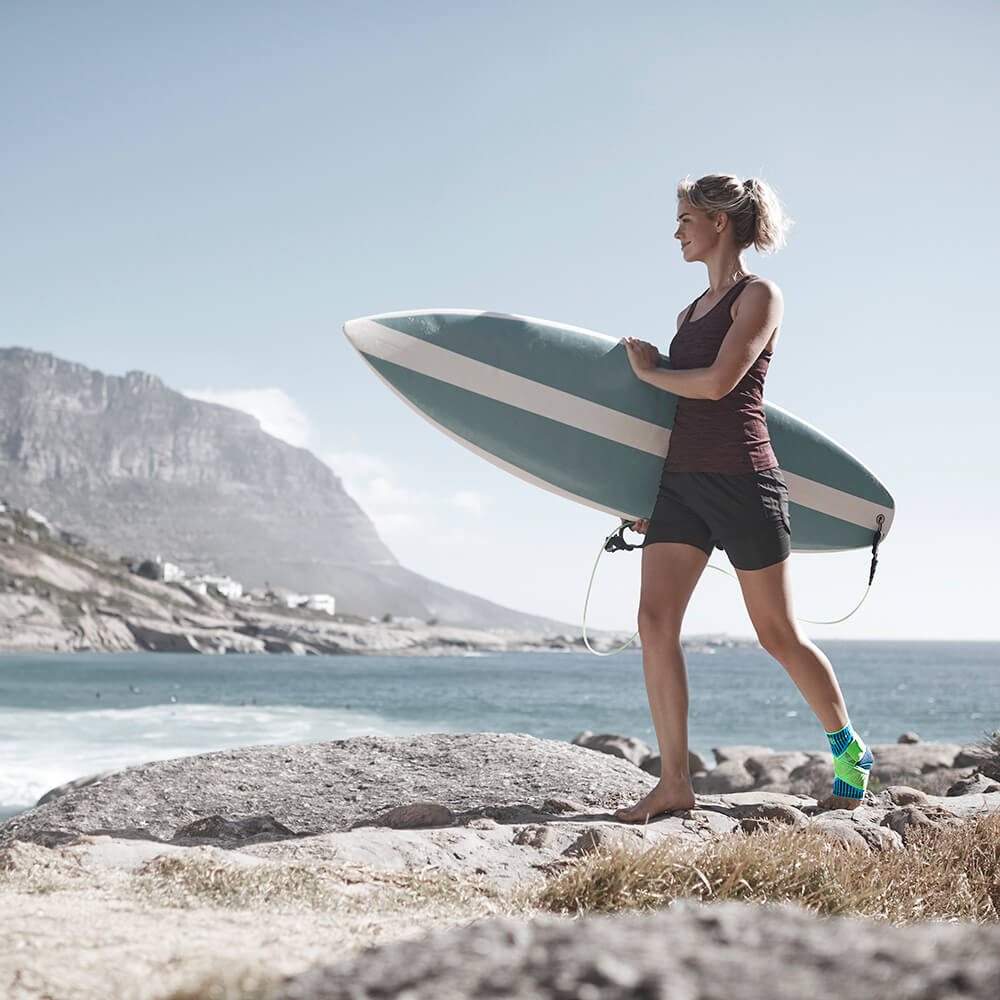 Woman carrying surfboard on rocky beach with mountain in background