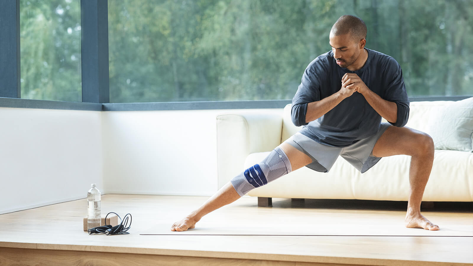 Image of a man wearing Bauerfeind's GenuTrain knee brace while stretching before an in-home workout.