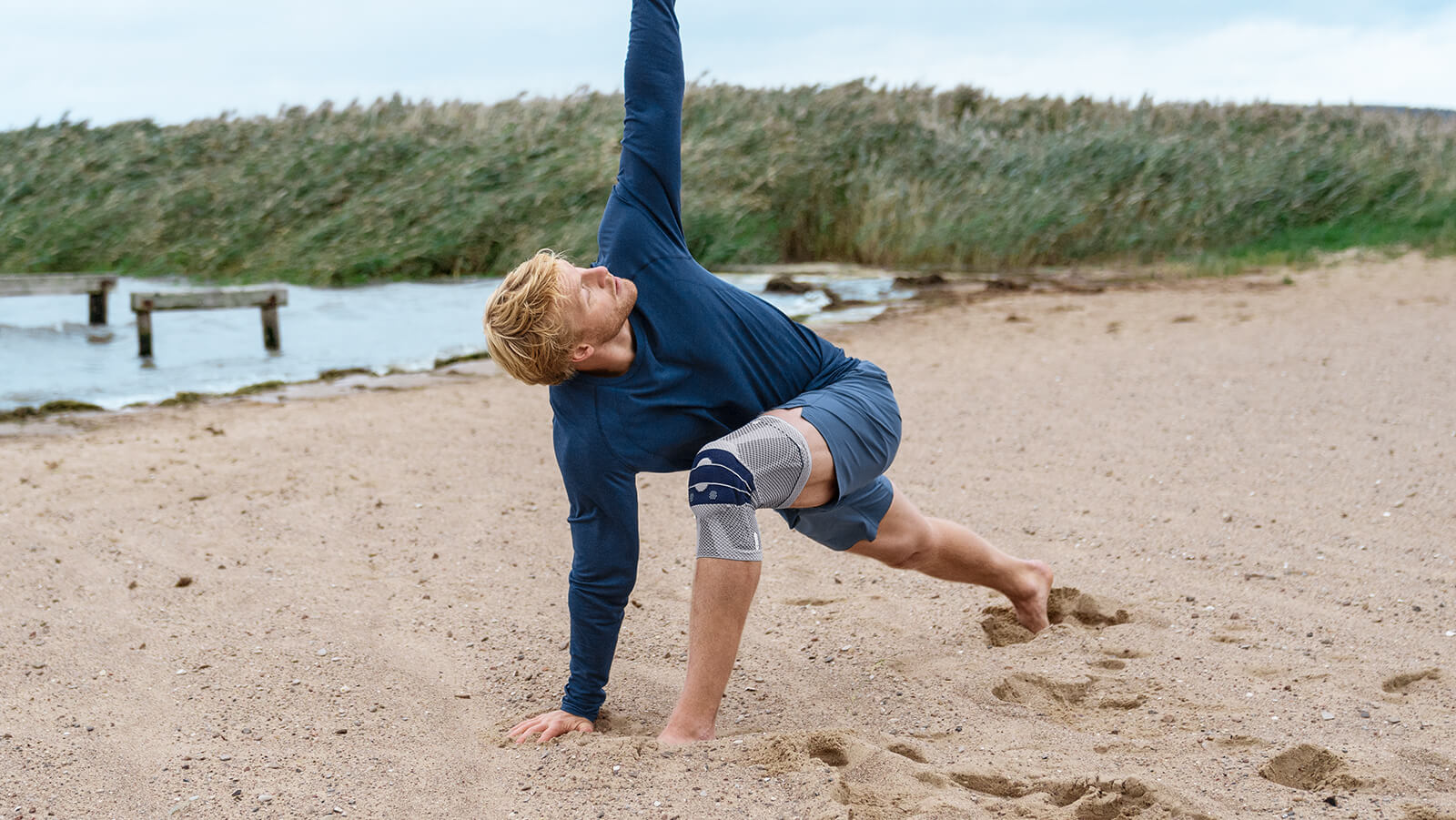 Man practicing yoga on the beach wearing Bauerfeind's GenuTrain knee brace.