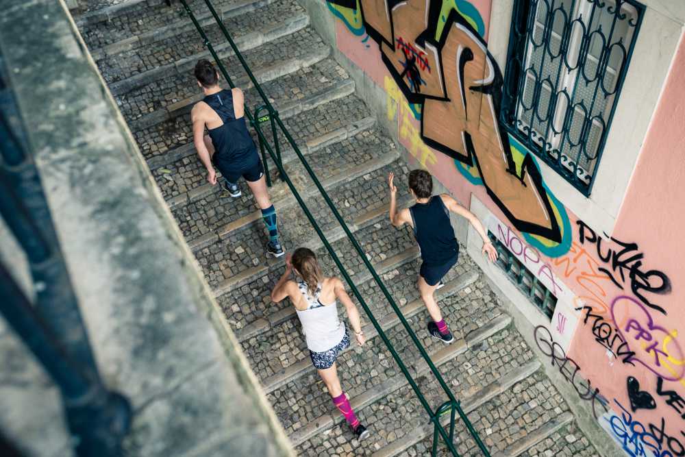 Three young adults wearing Bauerfeind's Run Performance Compression Socks while running uphill in an inner-city street.