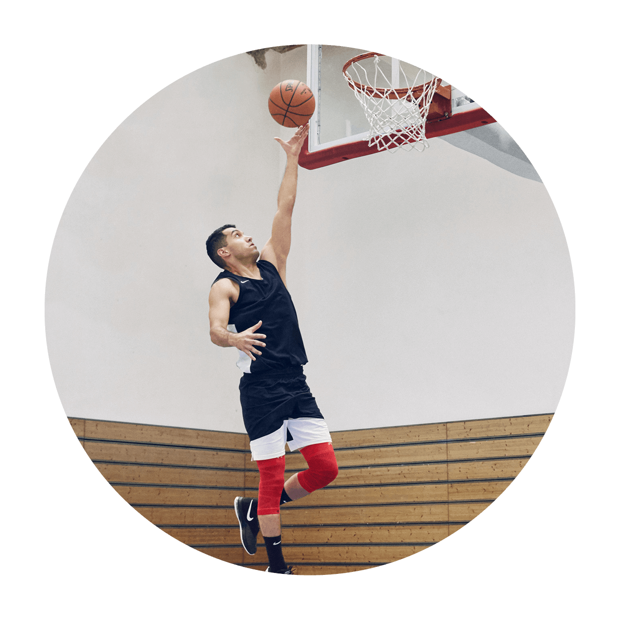 Athlete attempting a layup on an indoor basketball court while wearing Bauerfeind's Sports Compression Knee Support NBA Bulls Edition.