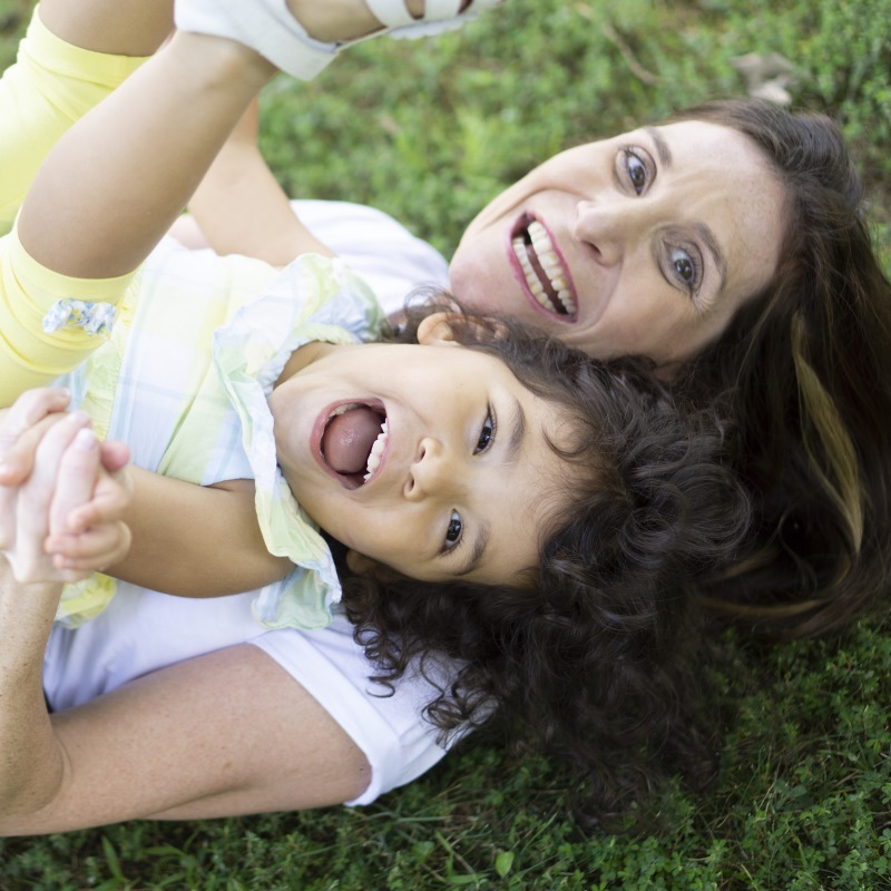 Mother and daughter playing and laughing together on grass, capturing a joyful moment outdoors.