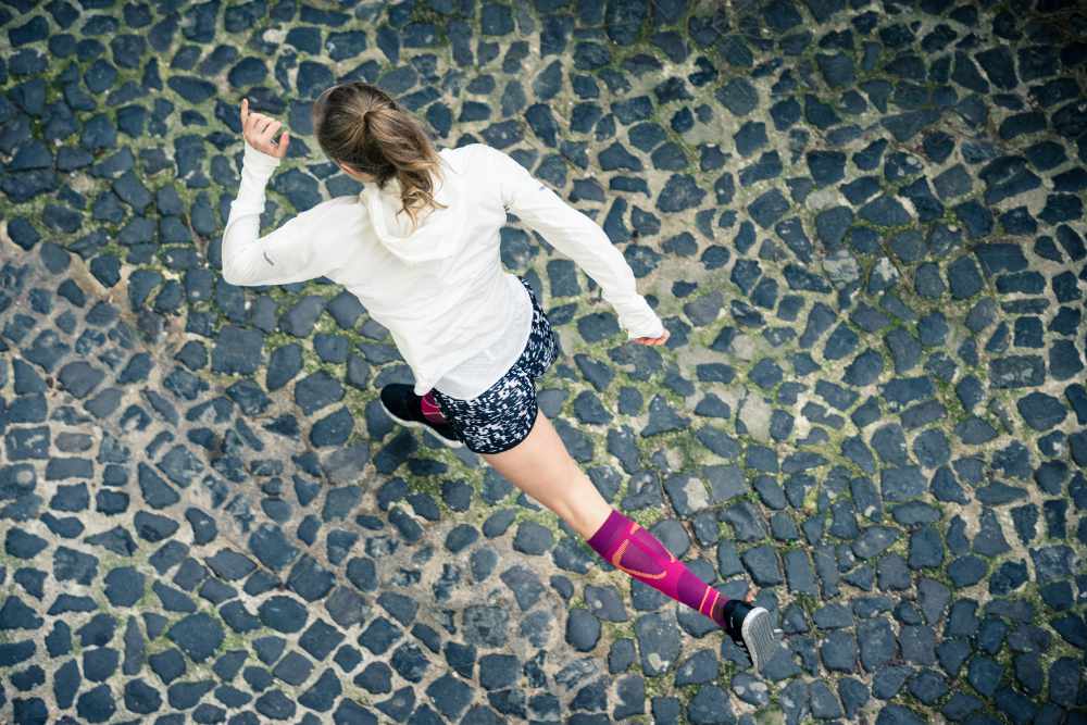 Woman wearing Bauerfeind's Run Performance Compression Socks while running through a city street.