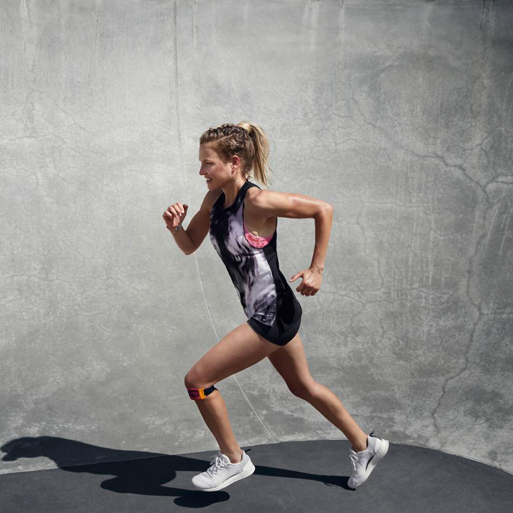 Woman running in front of a concrete wall wearing a Sports Knee Strap