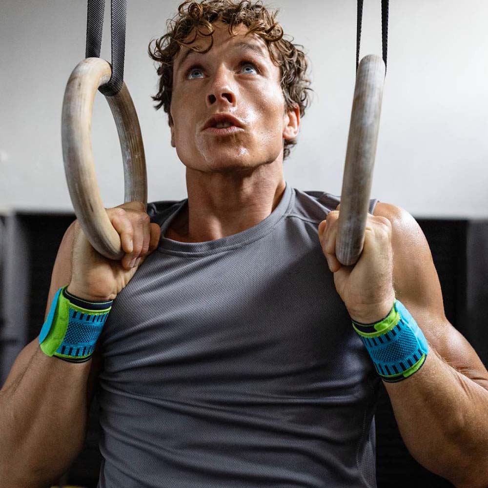 Man performing ring pull-ups while wearing Bauerfeind's Sports Wrist Strap during a fitness workout.