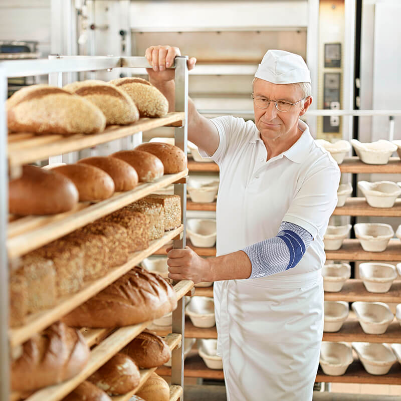 Image of senior baker in white uniform adjusting shelves stocked with various freshly baked bread with EpiTrain