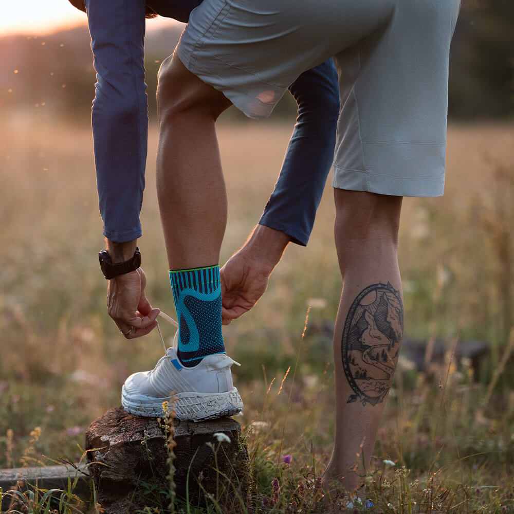 Man wearing the Sports Achilles Support in white sneakers teiing laces