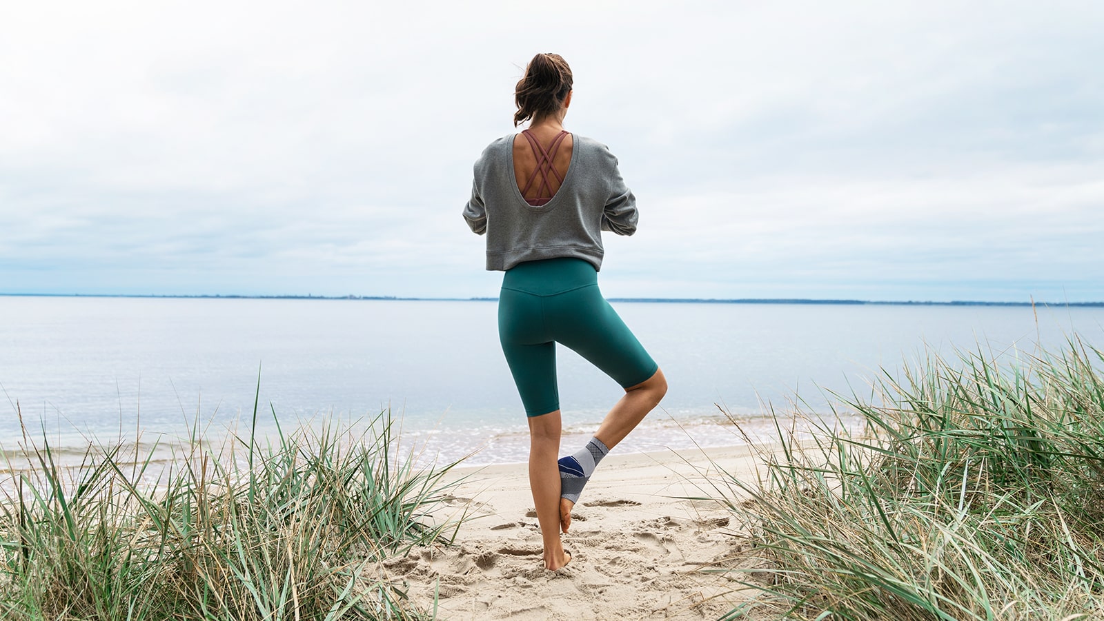 Woman practicing yoga near the ocean while wearing Bauerfeind's MalleoTrain S ankle brace.