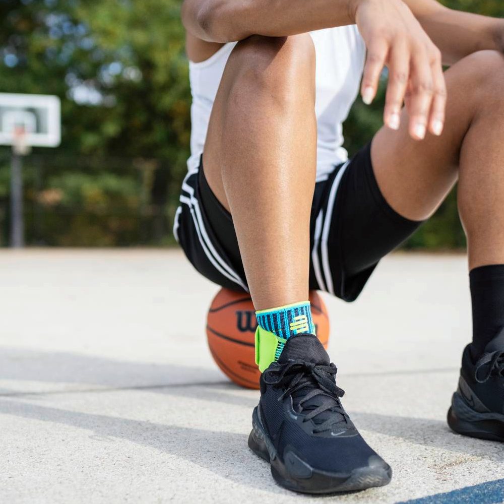 Basketball player wearing black sneakers and colorful socks sitting on an outdoor court with a ball