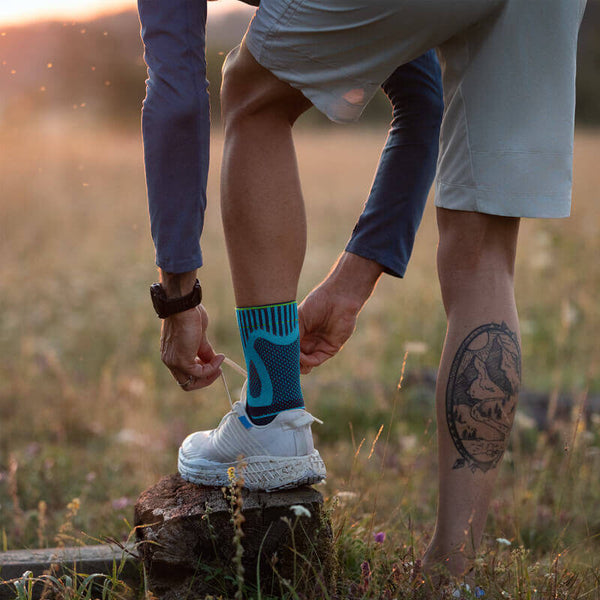 Man tying his shoes while wearing Bauerfeind's Sports Achilles Support before going on a morning jog through a grassy field.