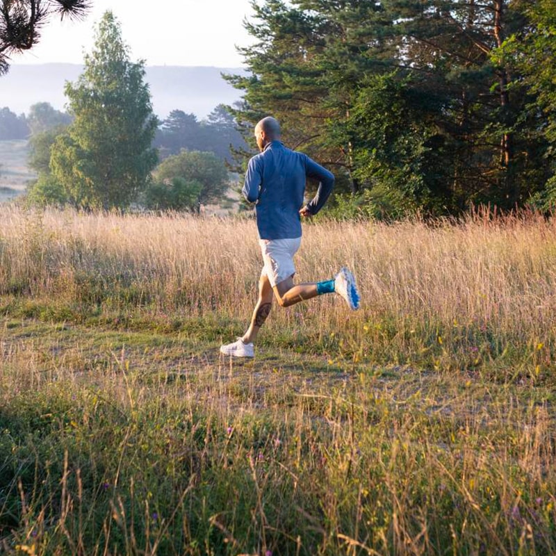 Man wearing Bauerfeind's Sports Achilles Support while on a morning run through a grassy field.