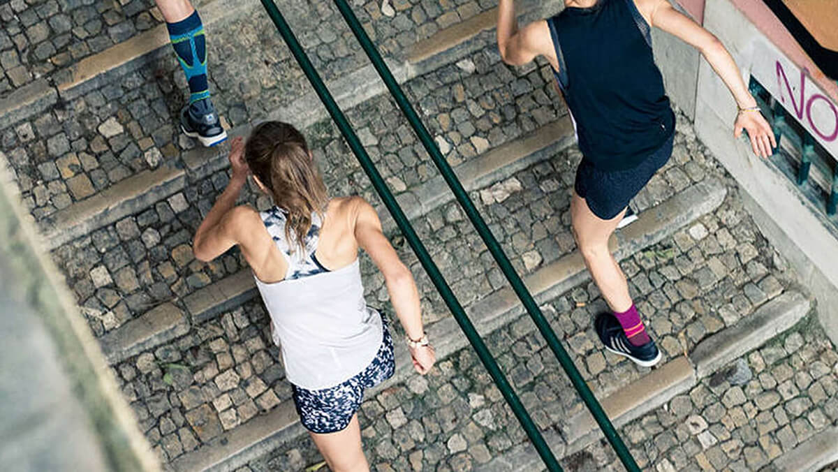 Two people running up a cobblestone staircase outdoors, focusing on their fitness training.